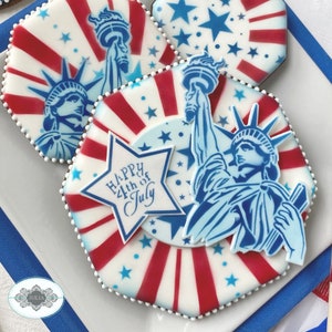 Puede incluir: Galletas patri&oacute;ticas decoradas con la Estatua de la Libertad, rayas rojas y blancas y estrellas azules. Las galletas est&aacute;n decoradas con glaseado blanco y el texto "Happy 4th of July" en una estrella.