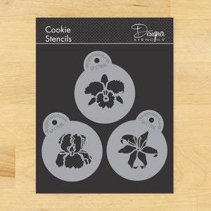 May include: A black cookie stencil set with three floral designs: an orchid, an iris, and a lily. The stencils are in circular frames with the text "designerstencils.com" and product codes. The top of the package reads "Cookie Stencils".