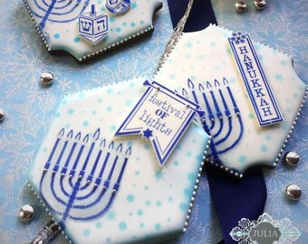Könnte beinhalten: Dekorierte Chanukka-Kekse mit blau-weißer Glasur. Die Kekse zeigen Menora, Dreidel und die Worte "Festival of Lights" und "Hanukkah". Die Kekse sind mit blauen Punkten und silbernen Dragees verziert.