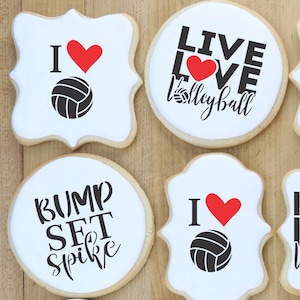 May include: Four decorated cookies with volleyball themes. The cookies are white with black and red designs. The designs include a volleyball, a heart, and the text "I love volleyball", "Live Love Volleyball", "Bump Set Spike", and "I heart volleyball".