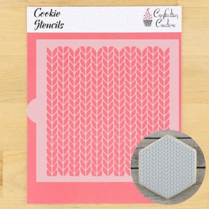 May include: A pink cookie stencil with a knitted pattern. The stencil is on a wooden surface and there is a sample cookie decorated with the stencil design.