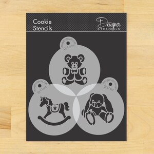 May include: A black cookie stencil set featuring three designs: a teddy bear with a bow tie, a rocking horse with a star, and a bunny. The words "Cookie Stencils" and "Designer Stencils" are printed on the top.