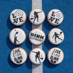 May include: Nine round cookies decorated with black and white designs. The cookies feature images of people playing pickleball and the words "Live Love Dink" and "Dink Responsibly".