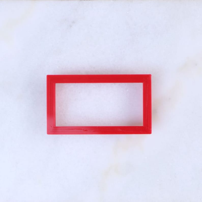 May include: A red plastic rectangular frame with a blank space inside. The frame is on a white marble surface.