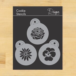 May include: A set of cookie stencils featuring floral designs. The stencils include a rose, a daisy, and a pansy, each within a circular frame. The text "Cookie Stencils" and "Designer Stencils" are visible.