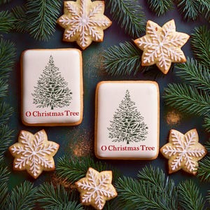Op de afbeelding: Overzichtsfoto van kerstkoekjes en dennentakken. Rechthoekige koekjes met witte glazuur hebben een groen kerstboomontwerp en de tekst "O Christmas Tree". Sneeuwvlokvormige koekjes met witte glazuur zijn ook aanwezig. De koekjes zijn gerangschikt op een donkergroen oppervlak.