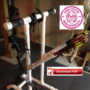 May include: White PVC pipe bow and arrow rack with a black bow and arrows. The rack has a horizontal bar for hanging the bow and two vertical pipes for storing arrows. The rack is labeled "Mom-Tested Mom-Approved".