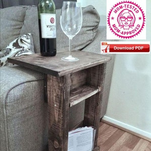 May include: A rustic wooden side table with a shelf and a magazine holder. The table is stained a dark brown colour and has a distressed finish. It is sitting next to a grey sofa.