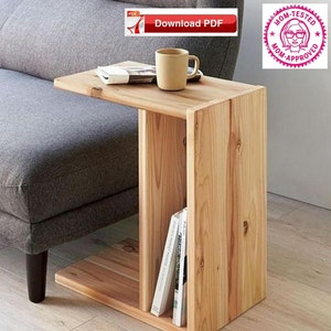 May include: A light wood side table with a shelf for books. The table has a small top surface that extends out to the side, making it perfect for a cup of coffee or a book.