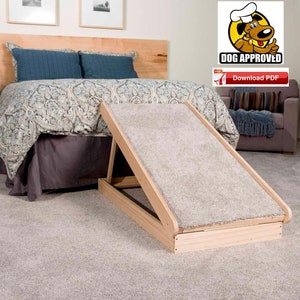 Puede incluir: Una rampa de madera para mascotas con una superficie alfombrada, diseñada para ayudar a las mascotas a subir y bajar de camas o muebles. La rampa está hecha de madera natural y tiene una construcción robusta. Se muestra en un entorno de dormitorio, junto a una cama con un edredón estampado.