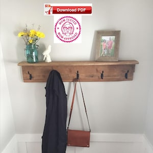 Może przedstawiać: Ruska drewniana półka z trzema haczykami, brązowa skórzana torebka wisząca na jednym haczyku i czarna kurtka wisząca na drugim haczyku. Na półce znajduje się oprawione zdjęcie i wazon z żółtymi kwiatami.