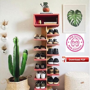 Puede incluir: Un zapatero rojo y de madera con 8 estantes, que contiene una variedad de zapatos. El zapatero está en una habitación con una planta de cactus en una cesta de mimbre, un taburete blanco y una impresión enmarcada de una hoja de monstera.