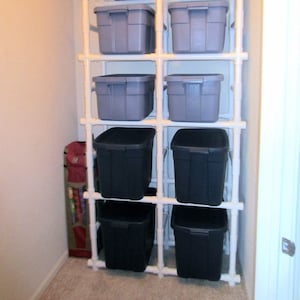 May include: A white PVC pipe storage rack with eight gray plastic storage bins. The rack is in a closet with a white door.