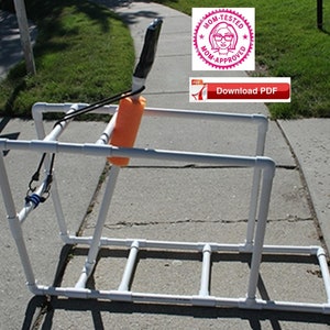 May include: A white PVC pipe frame with a black handle and an orange foam float. The frame is designed for a water sport activity. The image includes a pink and white sticker with the text "Mom-Tested Mom-Approved" and a red button with the text "Download PDF".
