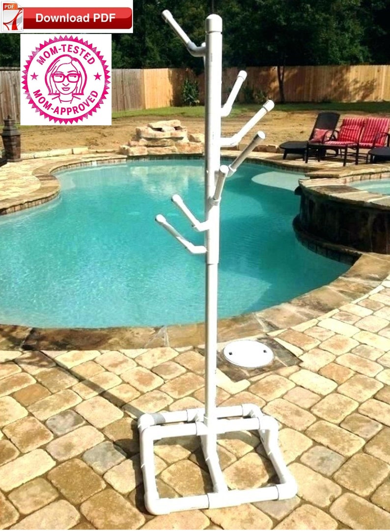 May include: White PVC pipe pool towel rack with multiple hooks. The rack is standing on a patio next to a swimming pool.