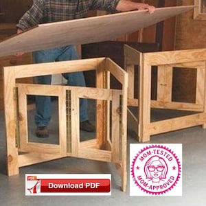 May include: A wooden folding table with a plywood top. The table is made of unfinished wood and has a simple design. The table is folded up and being held by a person. The table is labelled "Mom-Tested, Mom-Approved" and has a download PDF button.