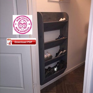 Puede incluir: Un zapatero de madera gris oscuro con cinco estantes montado en una pared dentro de un armario. El zapatero está inclinado para encajar en la esquina del armario. El zapatero está lleno de zapatos.