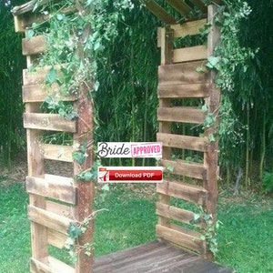 May include: A wooden pallet archway decorated with greenery and white flowers. The archway is standing on a grassy lawn. The text "Bride Approved!" is visible on a red sticker.