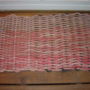May include: A woven doormat with a brown and pink rope design. The mat is made of thick, durable rope and has a textured surface.