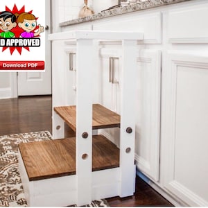 May include: White wooden step stool with two brown wooden steps. The stool is in a kitchen next to white cabinets with silver handles.