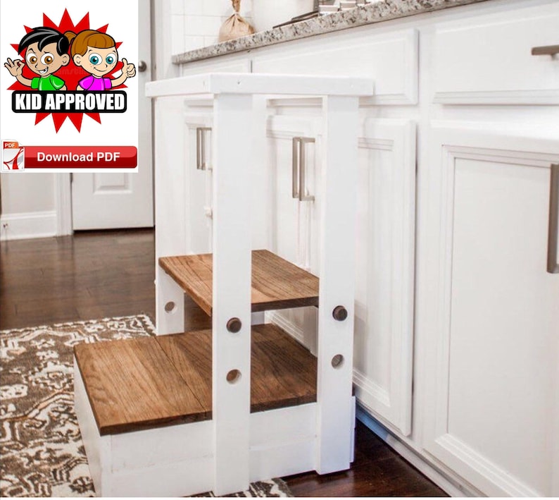 Puede incluir: Taburete de madera blanco con dos pelda&ntilde;os de madera marr&oacute;n. El taburete est&aacute; en una cocina junto a armarios blancos con tiradores plateados.