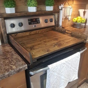 May include: A stainless steel stovetop with a wooden cutting board on top. The cutting board has a rustic brown finish and is made of wood planks. The stovetop has a digital display and four knobs.
