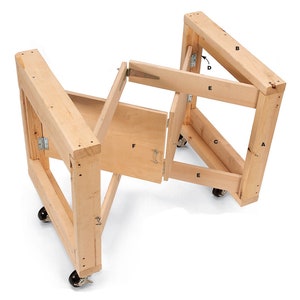 May include: A wooden folding workbench with four wheels and a hinged door. The workbench is made of natural wood and has a simple design. The workbench is labeled with letters A through F.