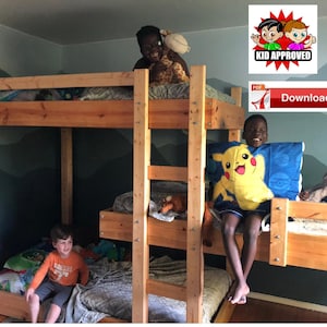May include: A triple bunk bed made of natural wood with three children on it. The top bunk has a stuffed giraffe, the middle bunk has a stuffed Pikachu, and the bottom bunk has a child sitting on a blanket. The wall behind the bunk bed is painted a light blue with a mountain scene.
