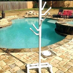 May include: White PVC pipe towel rack with multiple hooks, standing next to a swimming pool. The rack has a square base.