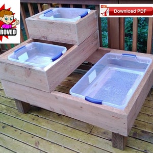 Puede incluir: Un arenero de madera con cuatro contenedores de plástico transparente, cada uno con un asa azul. El arenero está en una terraza de madera y tiene el texto "Kid Approved" en él.