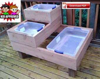 May include: A wooden sandbox with four clear plastic containers, each with a blue handle. The sandbox is on a wooden deck and has the text "Kid Approved" on it.