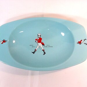 May include: A light blue oval ceramic ashtray with a walking man graphic and the text "BORN 1820 - STILL GOING STRONG".