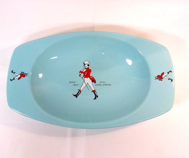 May include: A light blue oval ceramic ashtray with a walking man graphic and the text "BORN 1820 - STILL GOING STRONG".