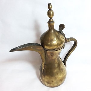 May include: A brass Arabic coffee pot with a domed lid and a spout. The pot has a decorative handle and a finial on the lid.