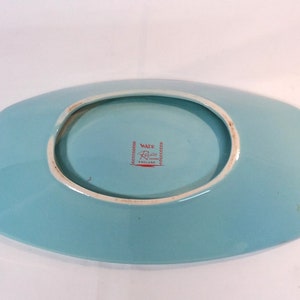 May include: A light blue ceramic serving dish with a raised rim and a slightly oval shape. The bottom of the dish has a red and white label that reads "Wade Regent England".