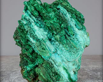 May include: A striking malachite specimen, showcasing a range of greens from deep to turquoise. The stone's surface is textured and layered, revealing its natural formation. The irregular shape of the mineral adds to its organic appeal. The image highlights the stone's natural beauty.