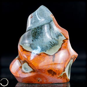 May include: A polished, freeform stone sculpture with a blend of colors. The top portion is a muted blue-green, speckled with darker spots. The lower section features warm orange and brown tones, creating a marbled effect. The sculpture has a smooth, glossy finish.