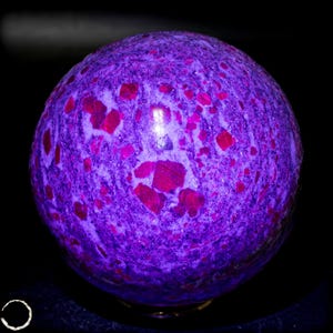 May include: A spherical stone with a polished surface featuring a vibrant purple base color speckled with numerous embedded deep red crystalline inclusions of varying shapes and sizes, creating a high-contrast textured appearance throughout.