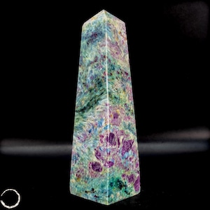 May include: A tall, obelisk-shaped crystal with a flat top. The stone features a mix of colors, including teal, purple, and green, with a speckled pattern. The crystal is standing upright against a black background.
