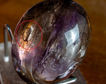 May include: A large, smooth, purple and brown crystal sphere with a swirling pattern. The sphere is sitting on a metal stand.
