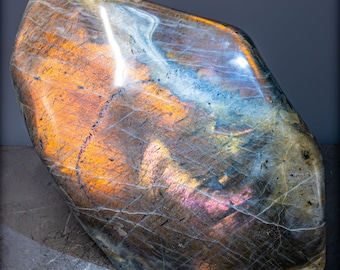May include: A large, iridescent labradorite gemstone with a smooth, polished surface. The stone displays a range of colors, including blue, green, gold, and purple.