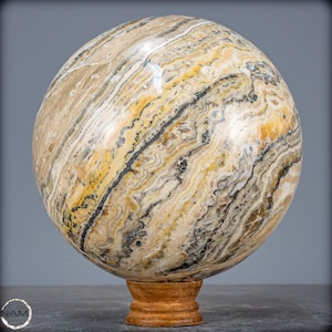 May include: A large, polished sphere of banded onyx with a swirling pattern of black, white, and yellow. The sphere is displayed on a wooden stand.