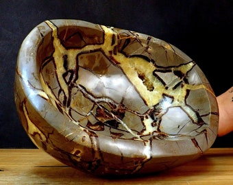 May include: A large, oval-shaped bowl made of brown and beige geode stone. The bowl has a natural, organic shape and a smooth, polished surface. The geode stone has a unique pattern of brown and beige veins and swirls.