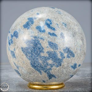 Op de afbeelding: Een bolvormig decoratief object met een gespikkeld grijs en blauw patroon. De bol staat op een goudkleurige basis. De algehele esthetiek is natuurlijk en elegant.