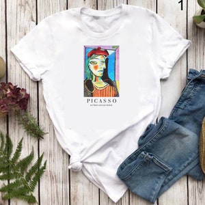 May include: White t-shirt featuring a colourful image of a woman's face by Pablo Picasso. The text "PICASSO der Maler und seine Modelle" is printed below the image.