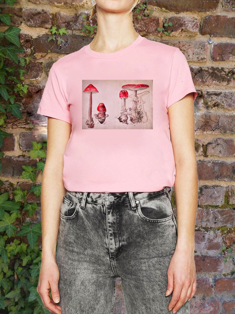 May include: Pink t-shirt with a graphic of red and white mushrooms on a beige background.
