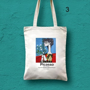 Puede incluir: Una bolsa de tela blanca con una imagen colorida de la cara de una mujer sobre un fondo rojo. El texto "Picasso The Late Work From the Collection of Jacqueline Picasso" est&aacute; impreso debajo de la imagen.