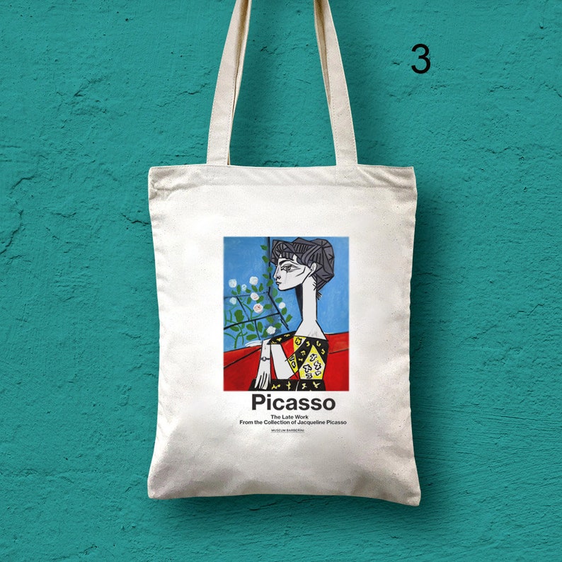 Puede incluir: Una bolsa de tela blanca con una imagen colorida de la cara de una mujer sobre un fondo rojo. El texto "Picasso The Late Work From the Collection of Jacqueline Picasso" est&aacute; impreso debajo de la imagen.