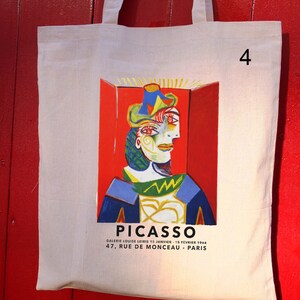 Puede incluir: Una bolsa de lona blanca con una pintura colorida de un rostro de Pablo Picasso. El texto "PICASSO" est&aacute; impreso en negro en la parte inferior de la bolsa, junto con la informaci&oacute;n de la galer&iacute;a: "GALERIE LOUISE LEIRIS 15 JANVIER - 15 FEVRIER 1964 47, RUE DE MONCEAU - PARIS". El n&uacute;mero "4" est&aacute; impreso en la esquina superior derecha de la bolsa.