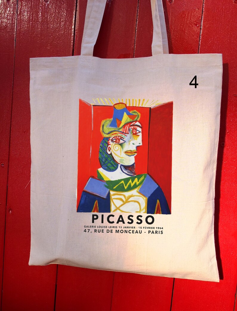 Puede incluir: Una bolsa de lona blanca con una pintura colorida de un rostro de Pablo Picasso. El texto "PICASSO" est&aacute; impreso en negro en la parte inferior de la bolsa, junto con la informaci&oacute;n de la galer&iacute;a: "GALERIE LOUISE LEIRIS 15 JANVIER - 15 FEVRIER 1964 47, RUE DE MONCEAU - PARIS". El n&uacute;mero "4" est&aacute; impreso en la esquina superior derecha de la bolsa.